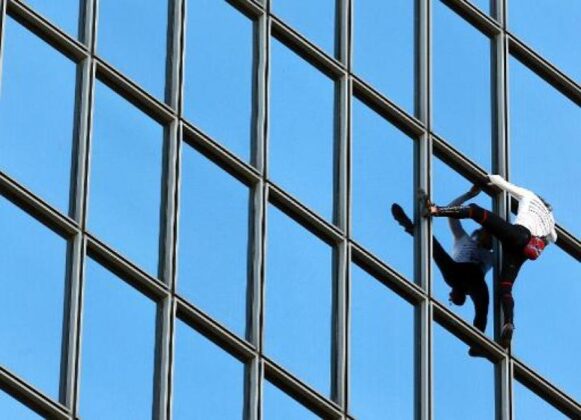 Defend Employees: Image is man crawling up side of mirrored building.